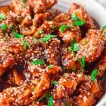 sesame chicken in a bowl with sesame seed topping and garnish