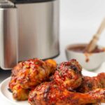 bbq chicken drumsticks sitting next to an air fryer and bowl of bbq sauce