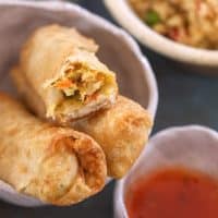 three egg rolls with dipping sauce with a bite taken from one