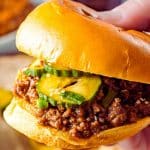 a hand holding a thick and juicy sloppy Joe sandwich with a golden bun