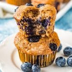 blueberry banana muffins stacked on top of each other with fresh blueberries all around the plate