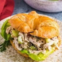 chicken salad sandwich with lettuce, pecans, celery, dill, and mayo on a croissant roll bun