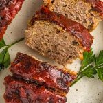 loaf of turkey meatloaf with a vibrant red glaze next to parsley garnish