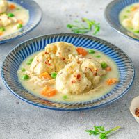 bowl of chicken and dumplings with peas, carrots, potatoes and garnish