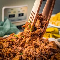 slow cooker pork butt being lifted with tongs